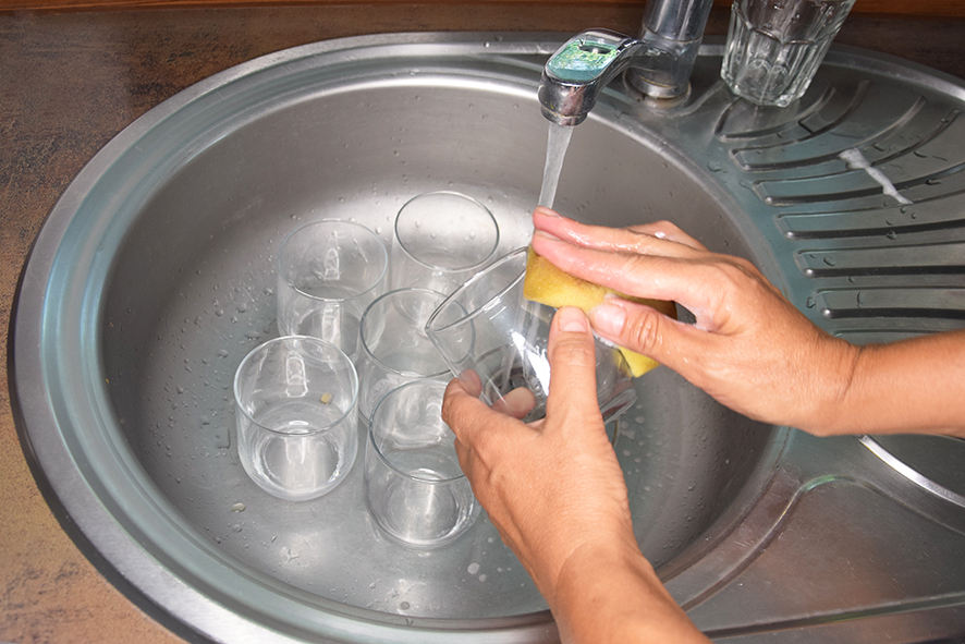 Žena v kuchynskom umývadle umýva poharíky na limonádu saponátom a vodou aby boli pripravené a čisté pred maľovaním.